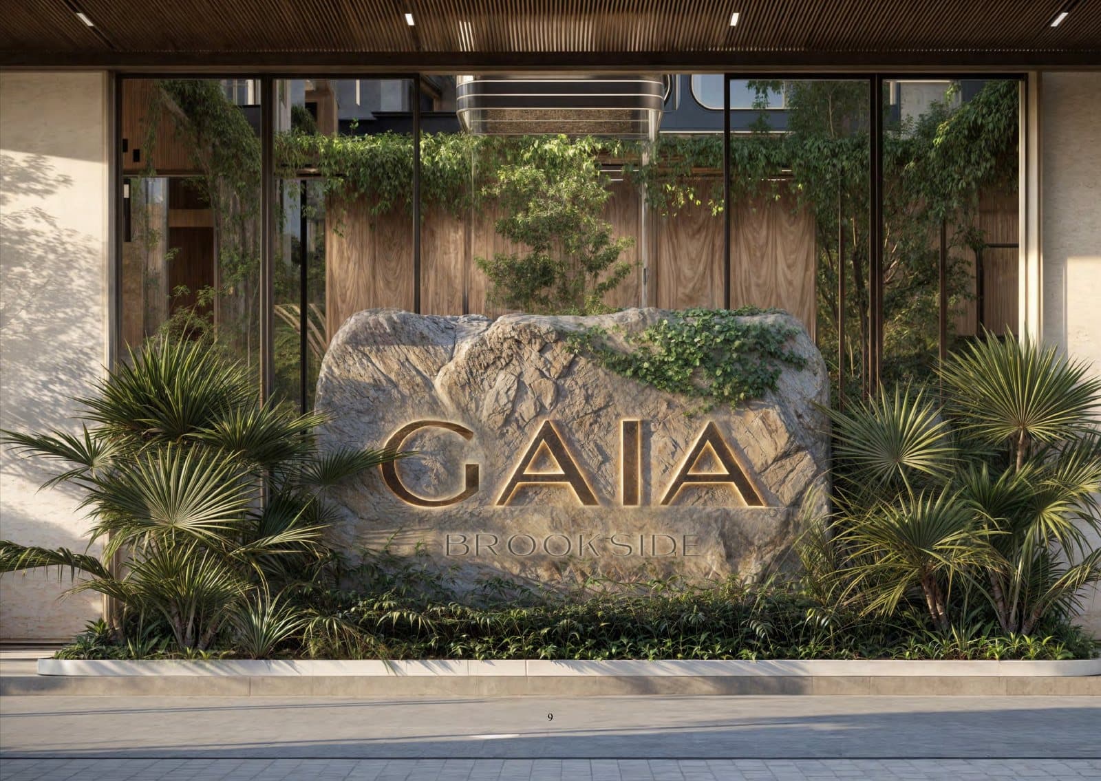 A boulder carved with the Gaia name among palms at the entrance